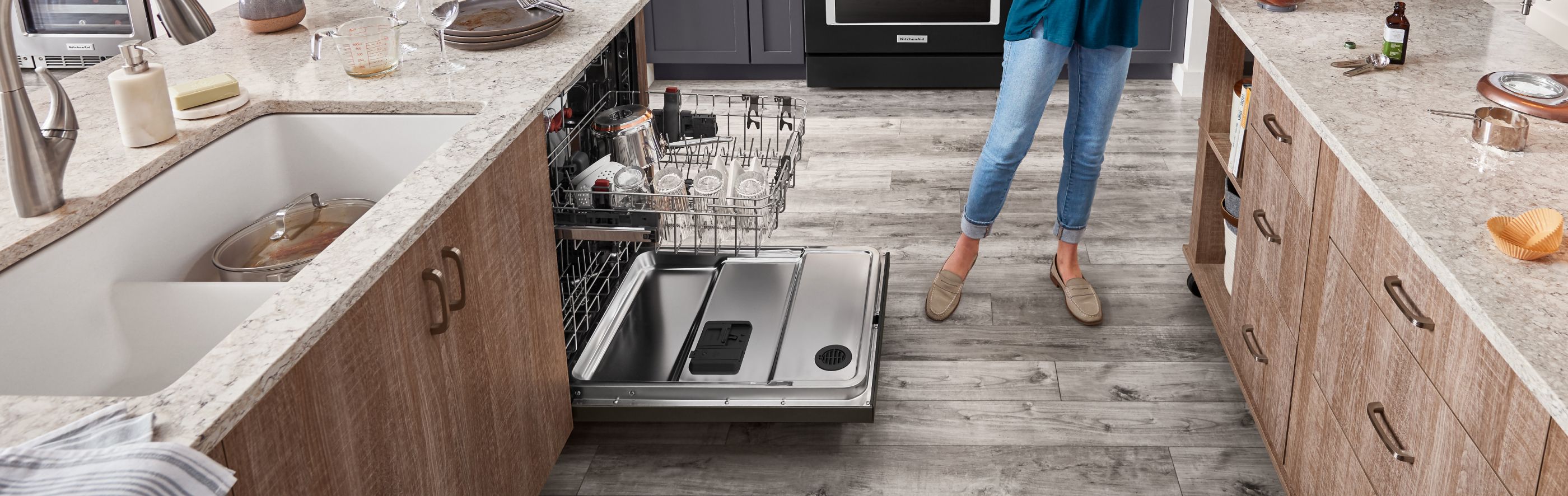 A woman standing next to an open KitchenAid® dishwasher in a modern kitchen