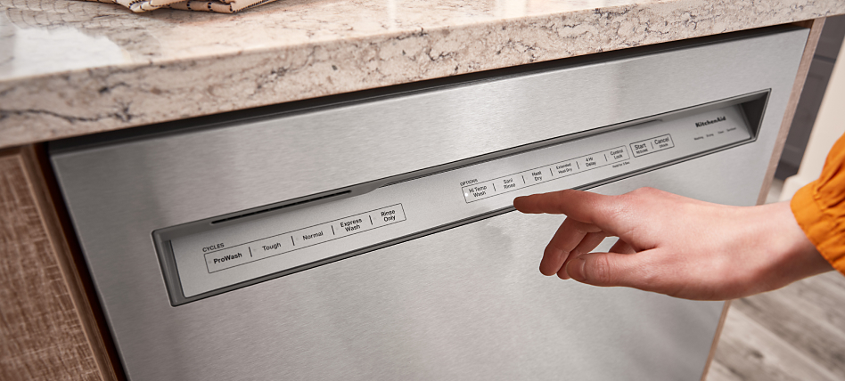 A close up of a woman programming a setting on the exterior of a KitchenAid® dishwasher