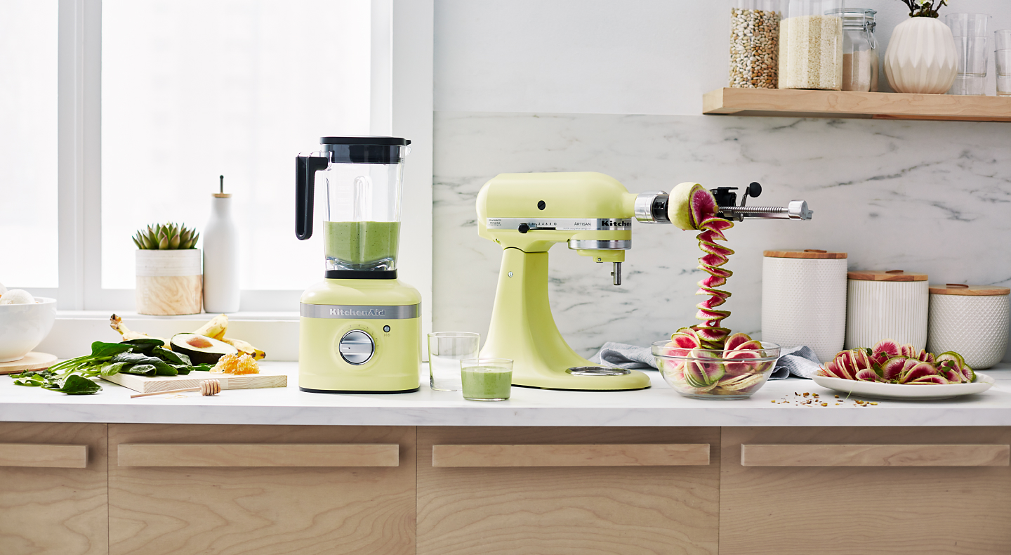 Green KitchenAid® stand mixer with spiralizer attachment, spiralizing fruit next to green KitchenAid® blender