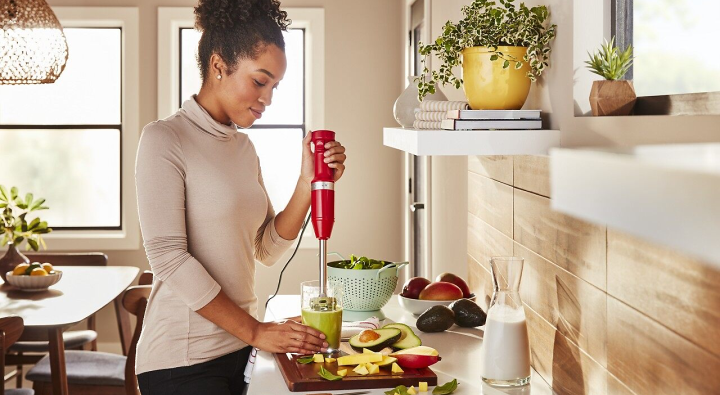 Person using red KitchenAid® immersion blender in cup