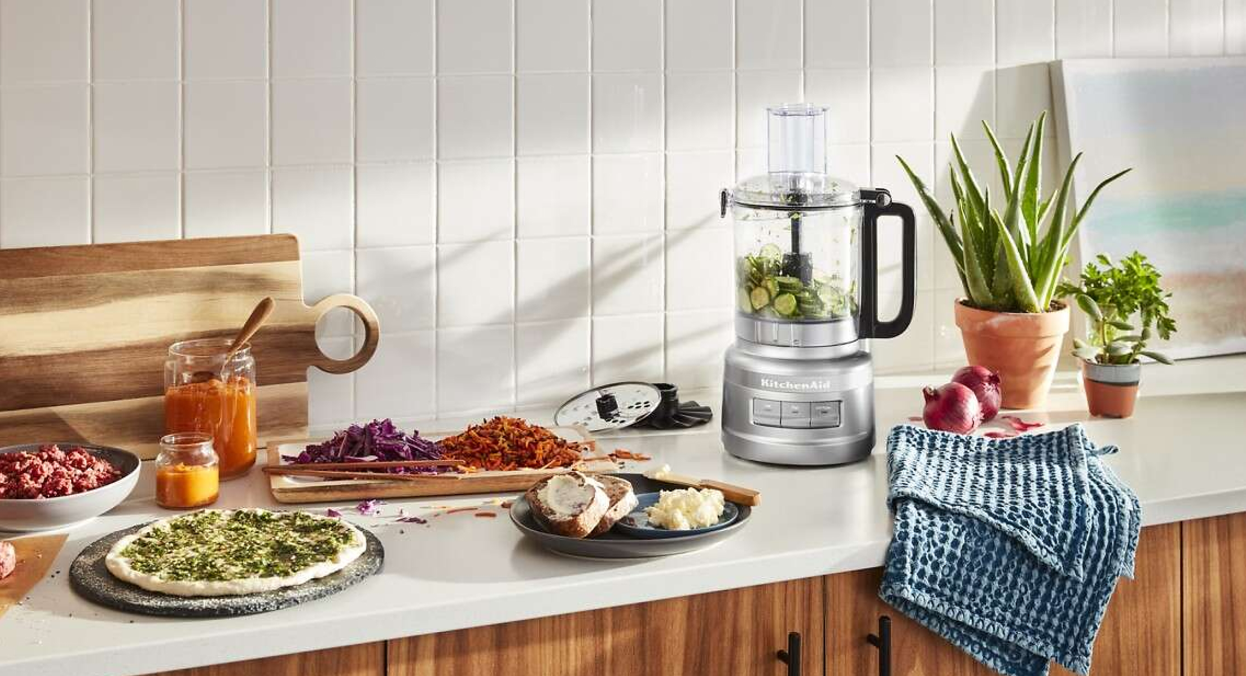 A bright kitchen with a food processor and food on the counter.