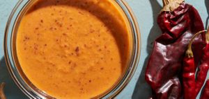 A bowl of perfectly pureed Mexican orange sauce speckled with seasoning sits next to various dried chilies that go into the recipe.