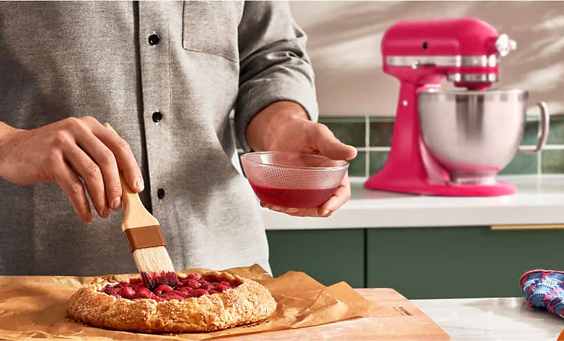 A person glazing a galette with hibiscus syrup with an Artisan® Stand Mixer in the background.