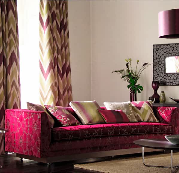 A bold fuschia couch in a living room with bright pillows, surrounded by bold decor pieces.