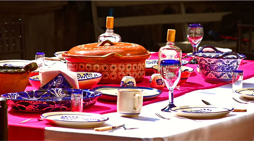 Une table dressée avec un chemin de table fuchsia, des bols colorés et de la vaisselle à motifs.