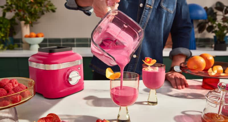 A person pouring a blended hibiscus drink from the K400 Hibiscus Blender into stylish cups with orange peel garnishes.