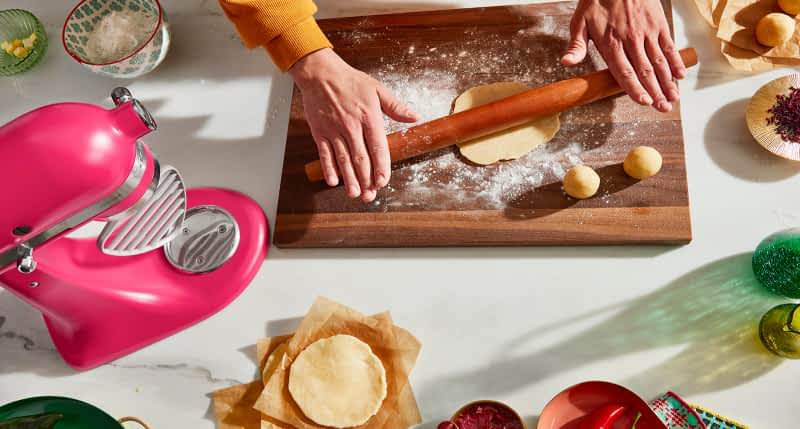A person rolling dough on a cutting board with a Hibiscus Artisan® Series Stand Mixer on the counter.