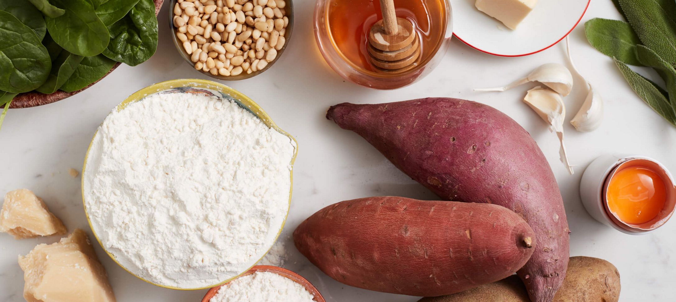 White Countertop with various ingredients, including fresh basil, garlic, flour, sweet potates, flour and honey