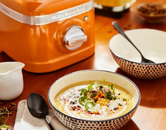 A decorative bowl of soup next to a K400 Variable Speed Blender in Honey.