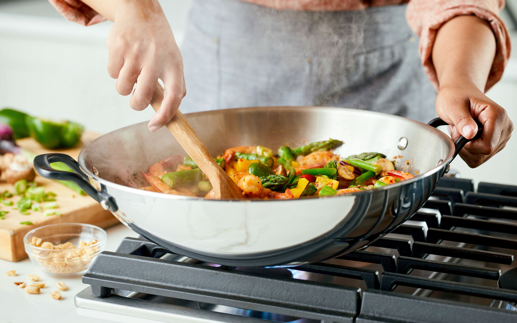 A person cooking with a stainless steel 5-ply base pan.