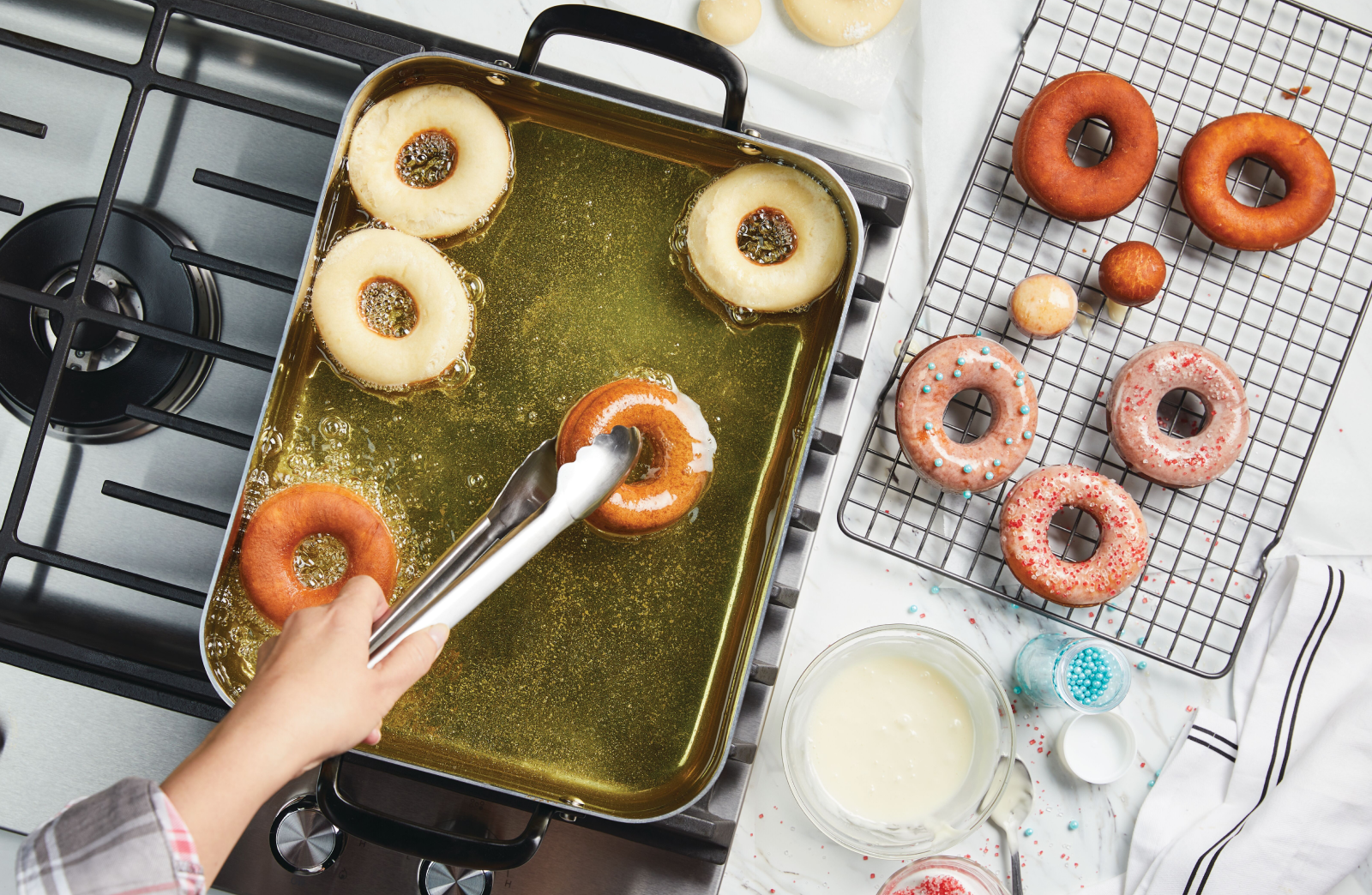 A person frying donuts in a KitchenAid® roasting pan filled with oil.