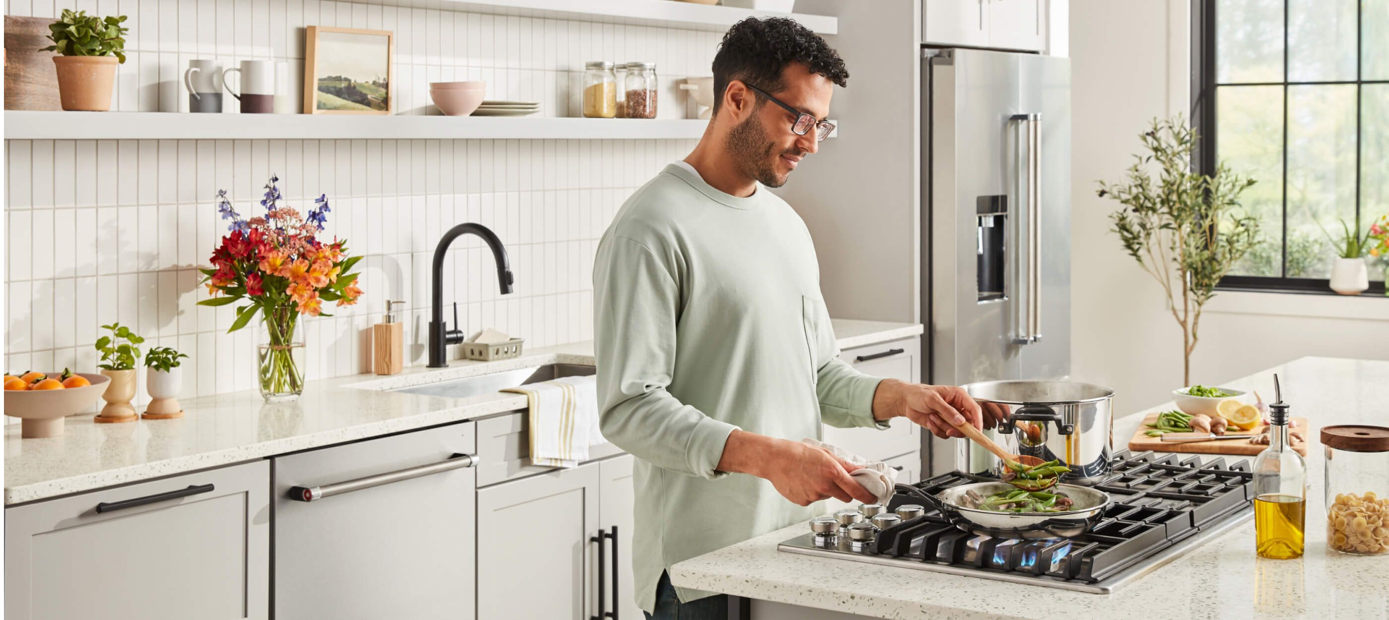 A person cooking over a cooktop in a bright, clean kitchen.