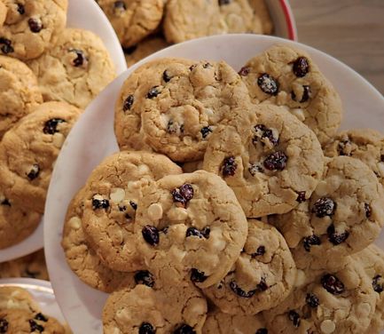 Four batches of freshly made brown butter white chocolate cookies on overlapping white plates.