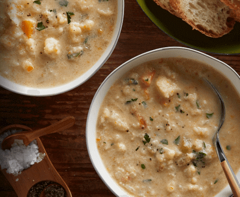 An overhead close-up of two bowls of cauliflower soup topped with fresh garnish.