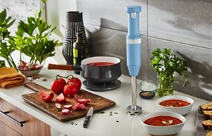 A KitchenAid Blue Velvet Cordless Immersion Blender standing upright on a bright kitchen countertop.