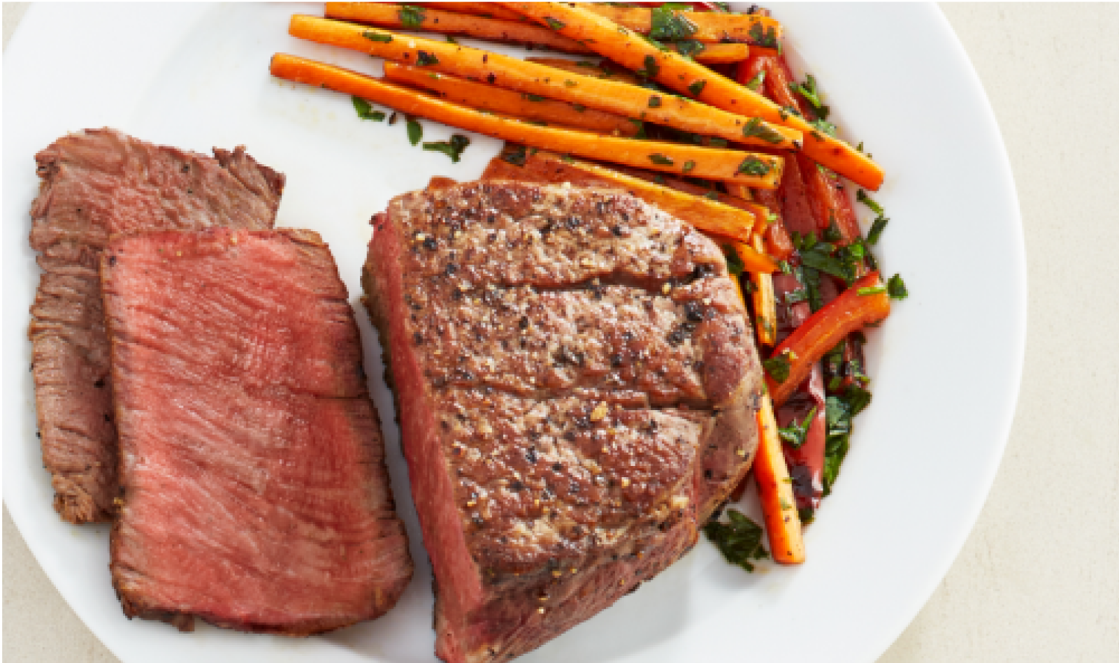 A medium rare steak on a plate with prepared carrots garnished with parsley. 