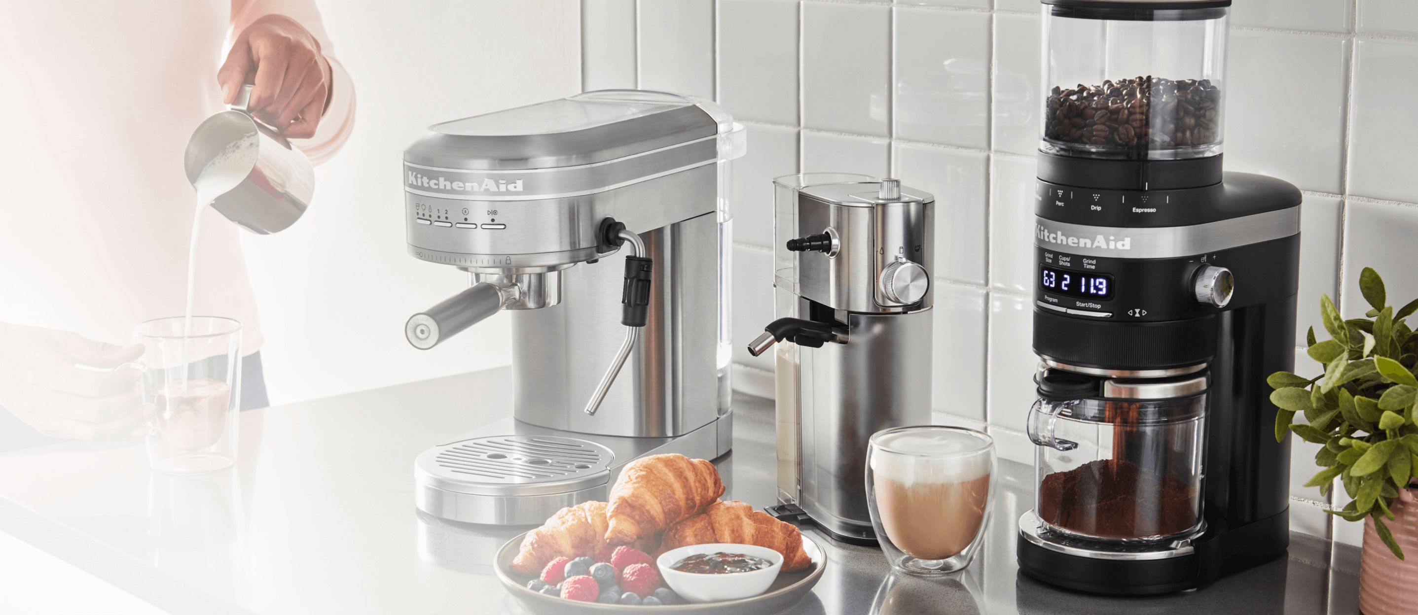 A KitchenAid® espresso machine, milk frother and burr coffee grinder on a countertop preparing espresso drinks. 
