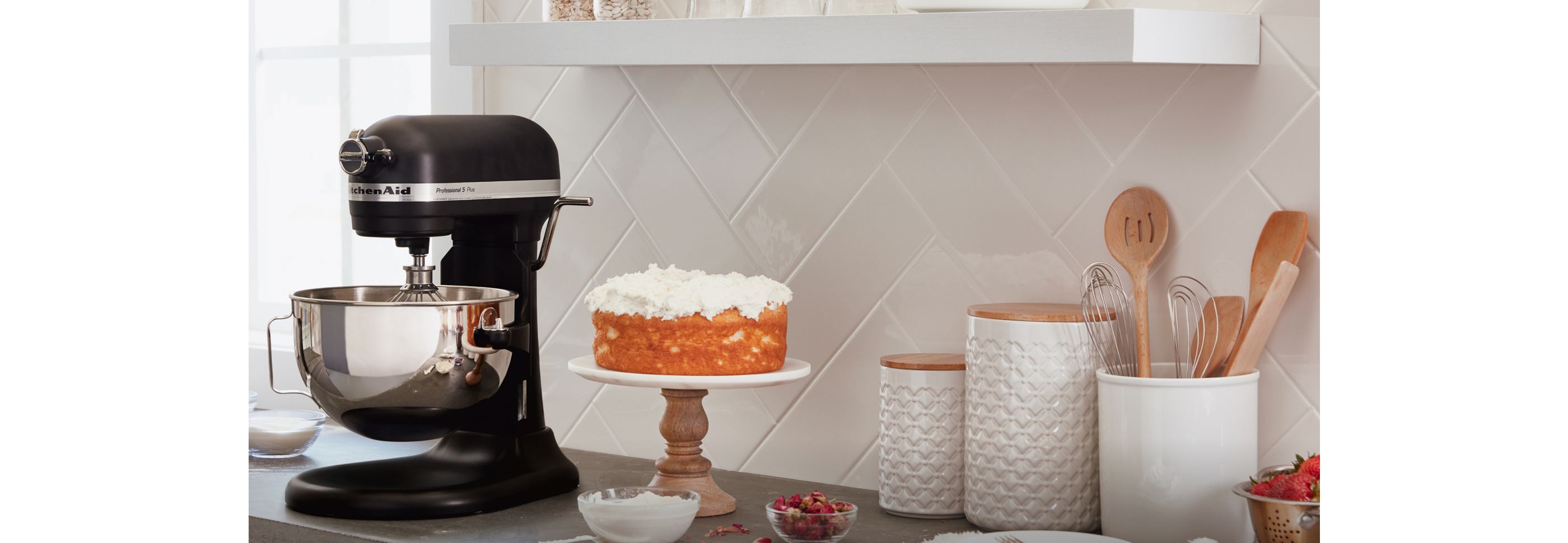 A KitchenAid® Stand Mixer on counter beside a cake