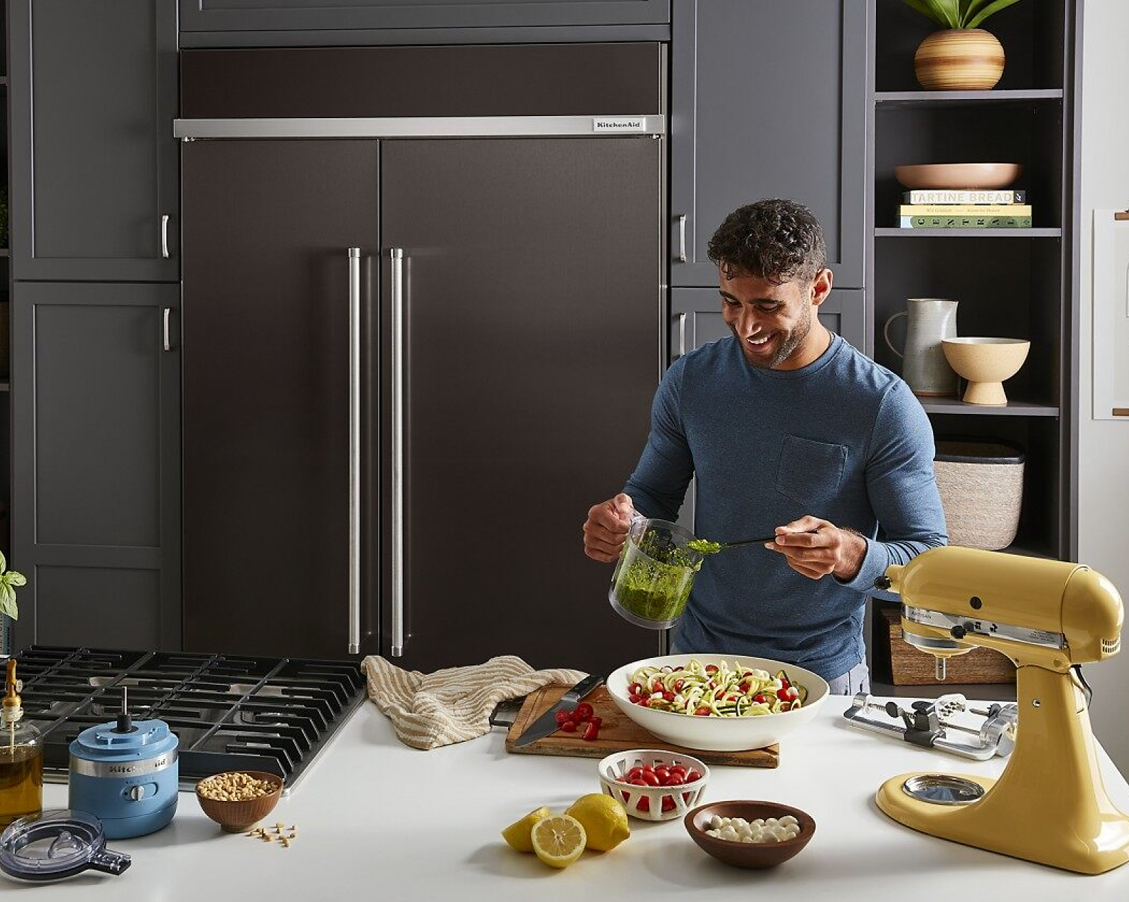 A person in a kitchen filled with a suite of KitchenAid® appliances, making a pesto Caprese pasta with zucchini noodles.