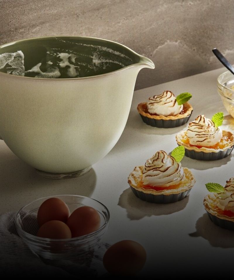 A KitchenAid® Stand Mixer ceramic bowl next to prepared dessert tarts.