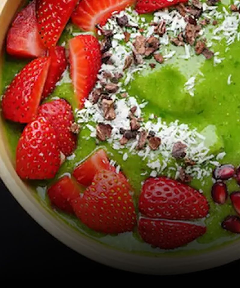 A green acai bowl garnished with fresh strawberries, shaved coconut and nuts.