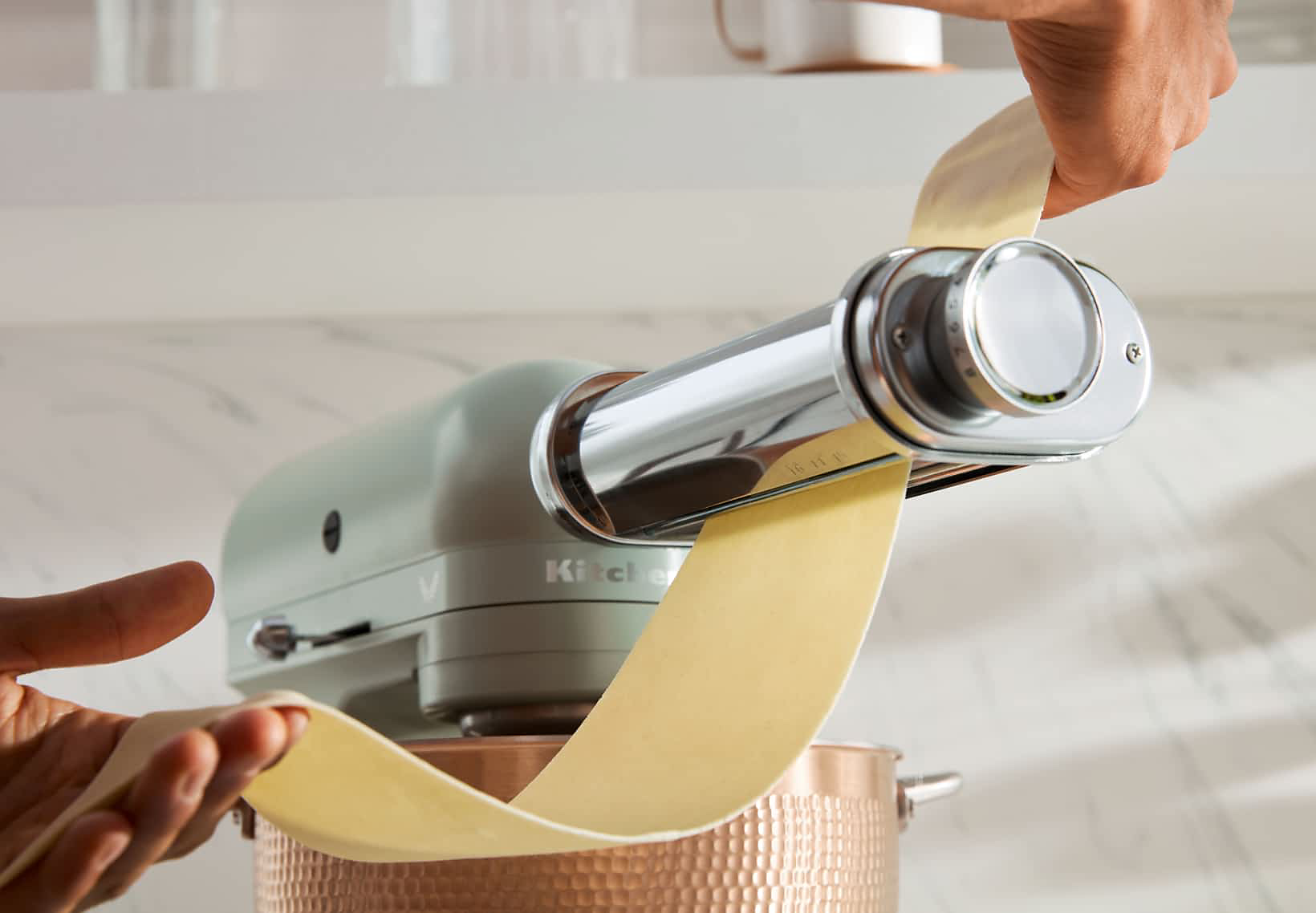 A maker making pasta using the pasta maker attachment on a Blossom Stand Mixer.