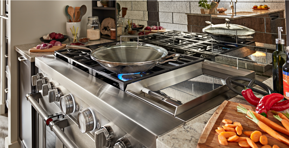 An ignited gas range with vegetables on the counter.