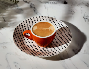 A cup of Espresso served on a black and white patterned dish.