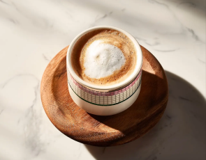 A macchiato served in a patterned cup on a wooden coaster.