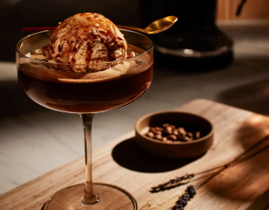 An affogato served in a coupe glass on a cutting board with espresso bean garnishes. 