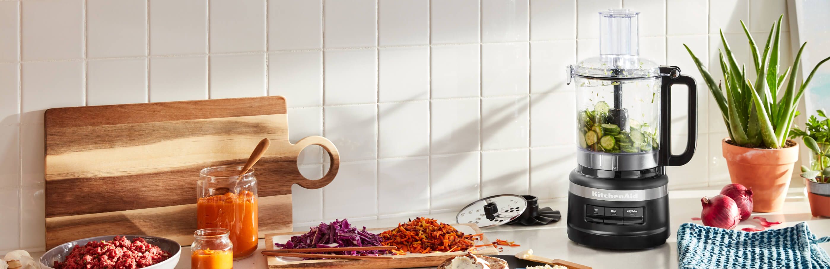 Robot culinaire KitchenAid® blanc sur un comptoir en bois avec des bleuets et autres ingrédients.