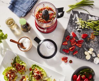 A Red KitchenAid® food chopper holding a red sweet pepper salsa for fresh lettuce wraps.