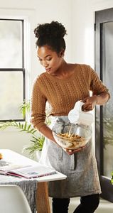 A woman mixing cookie batter in a clear glass bowl with a White Cordless Hand Mixer.