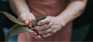 A person gently packing rice into a steamed banana leaf.