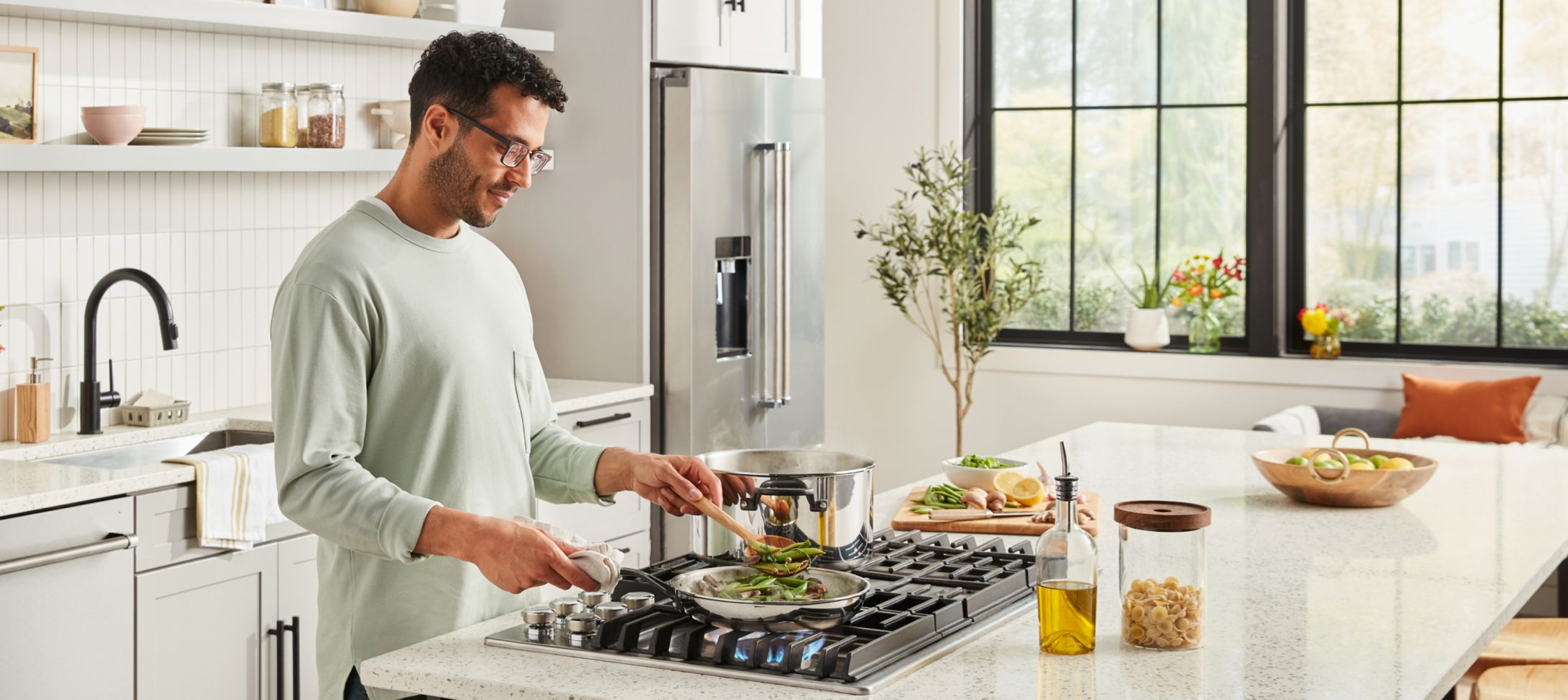 A person cooking over a cooktop in a bright, clean kitchen.