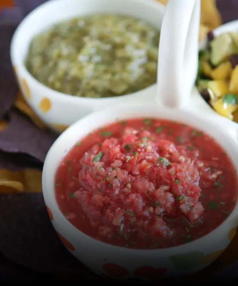 A three-bowl holder serving salsa, salsa verde and mango salsa on top of colored chips.