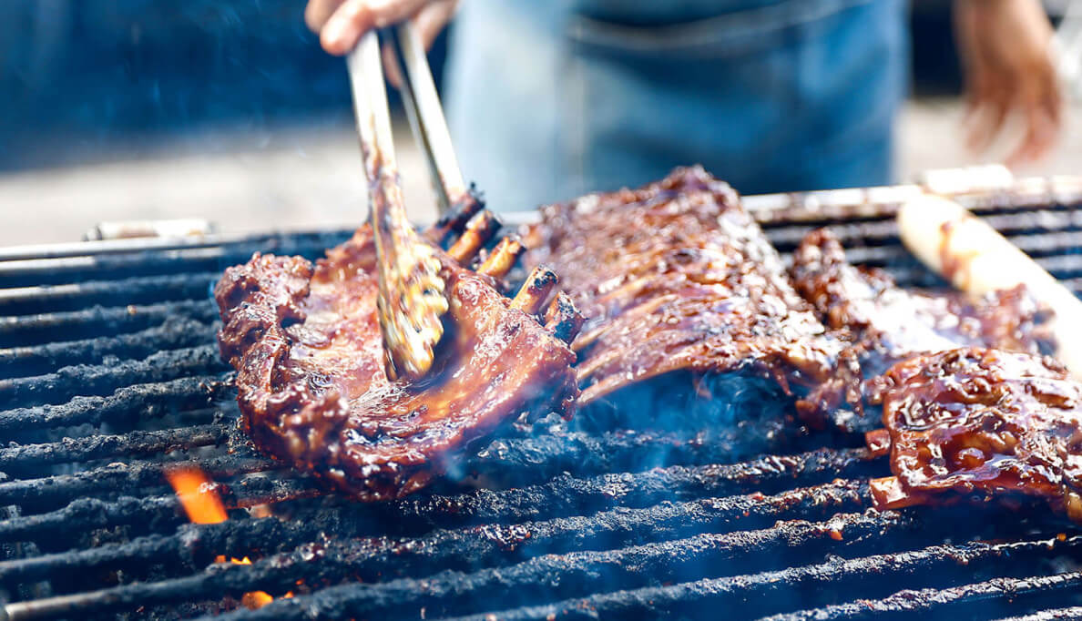 A rack of juicy ribs being turned over by tongs on a hot grill.