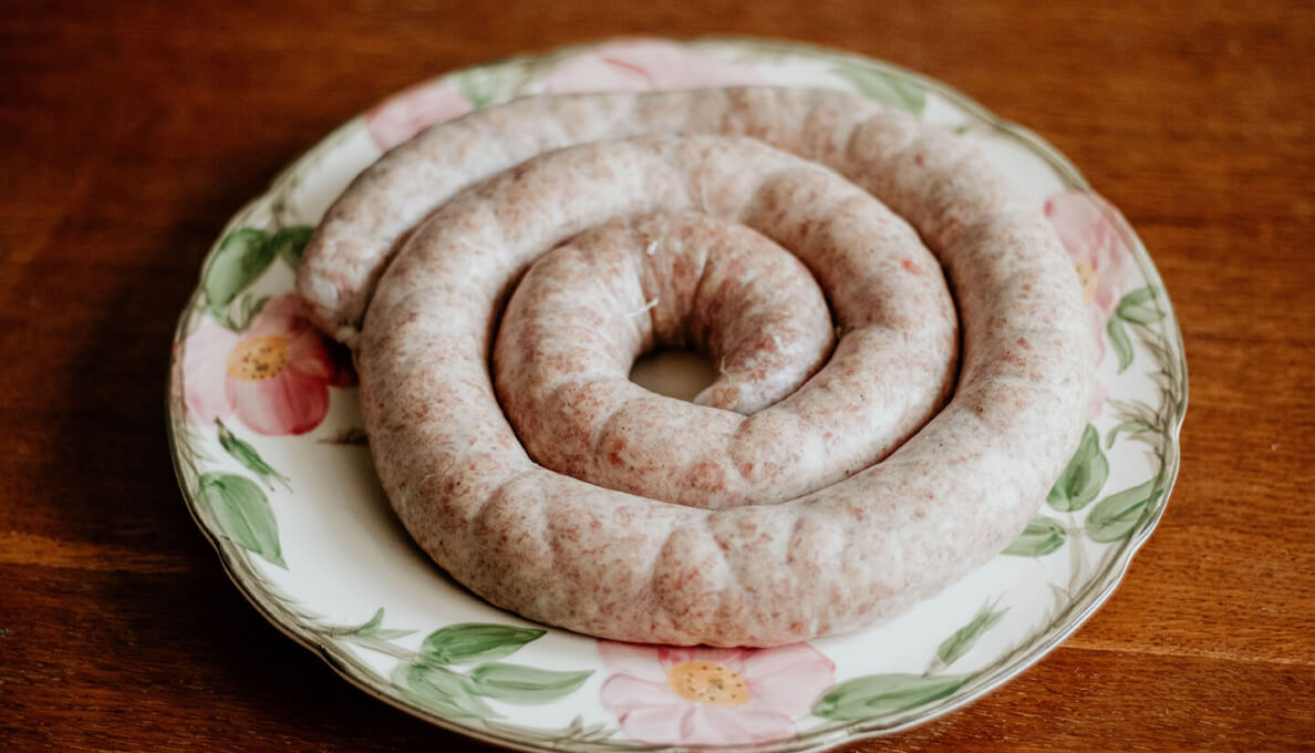 Freshly made sausage resting on a floral china plate.