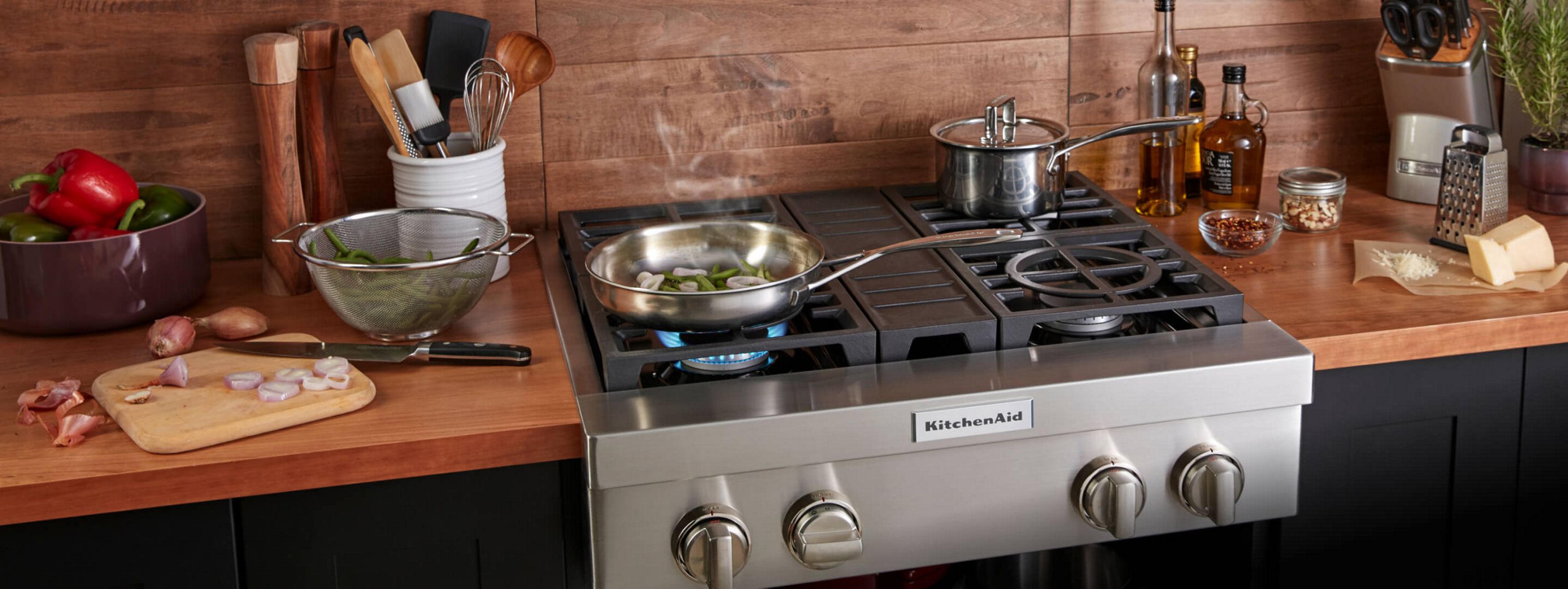 A KitchenAid® rangetop with vegetables simmering and a pot cooking.