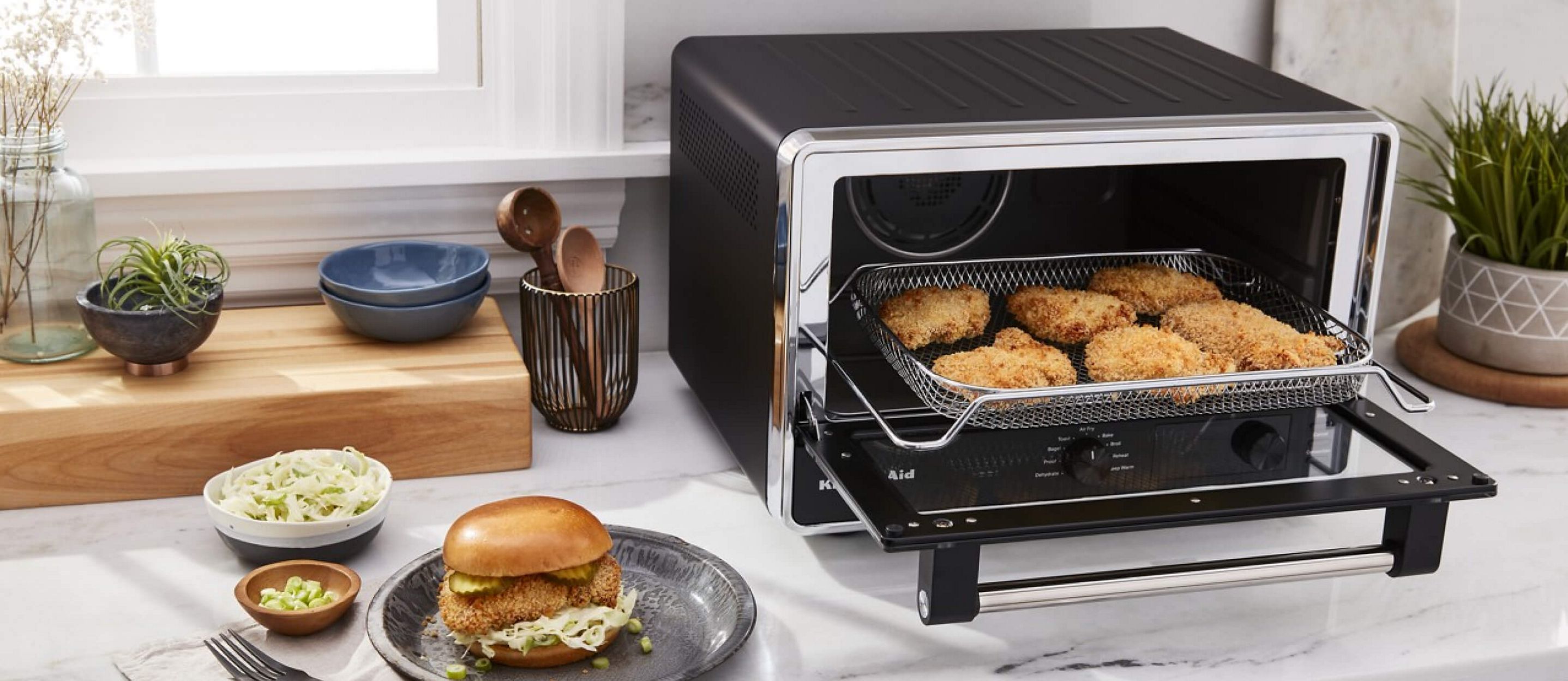 A Digital Countertop Oven with Air Dry cooking crispy chicken and a crispy chicken sandwich sitting on a plate with ingredients next to it.