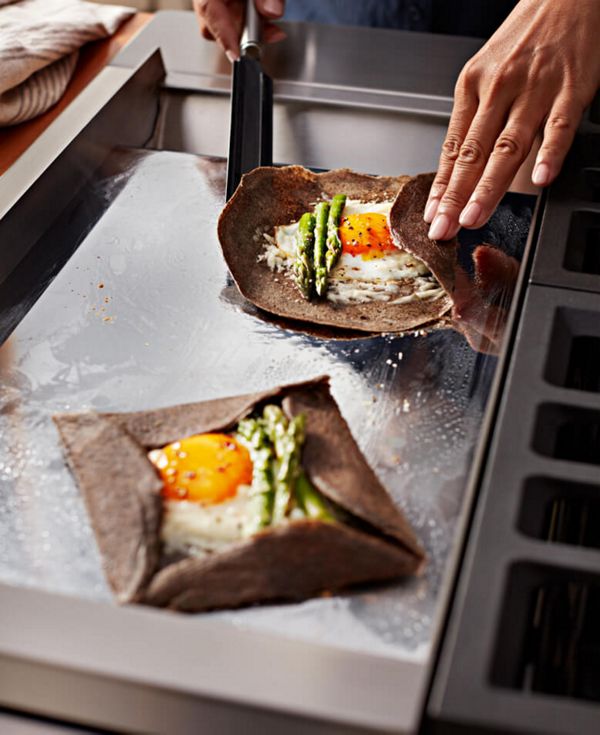 Sunny-side up eggs and asparagus being wrapped in a tortilla on the griddle.