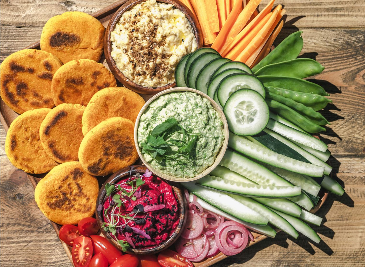A vegan charcuterie board filled with different hummus dips, vegetables and breads.