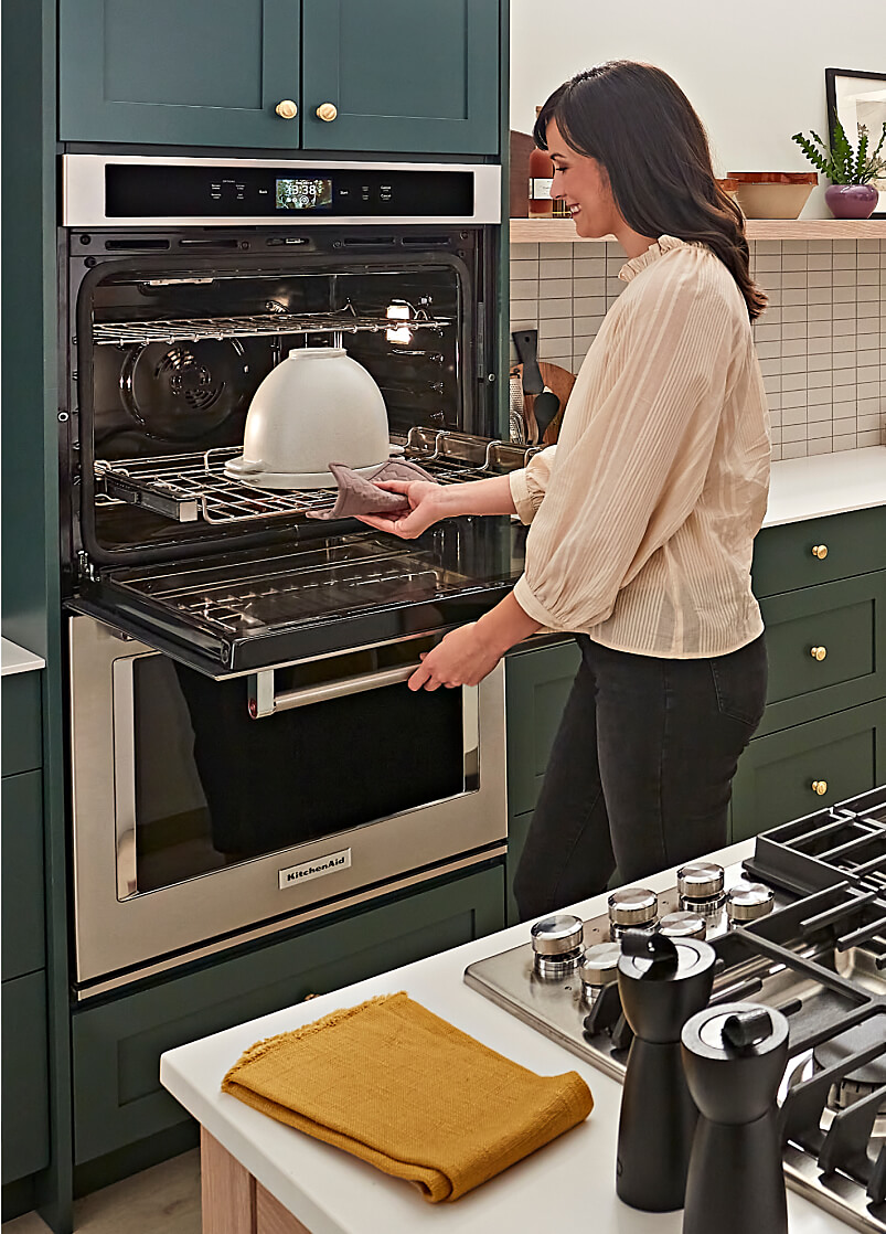 A person removing a bread bowl with lid from a double wall oven. 
