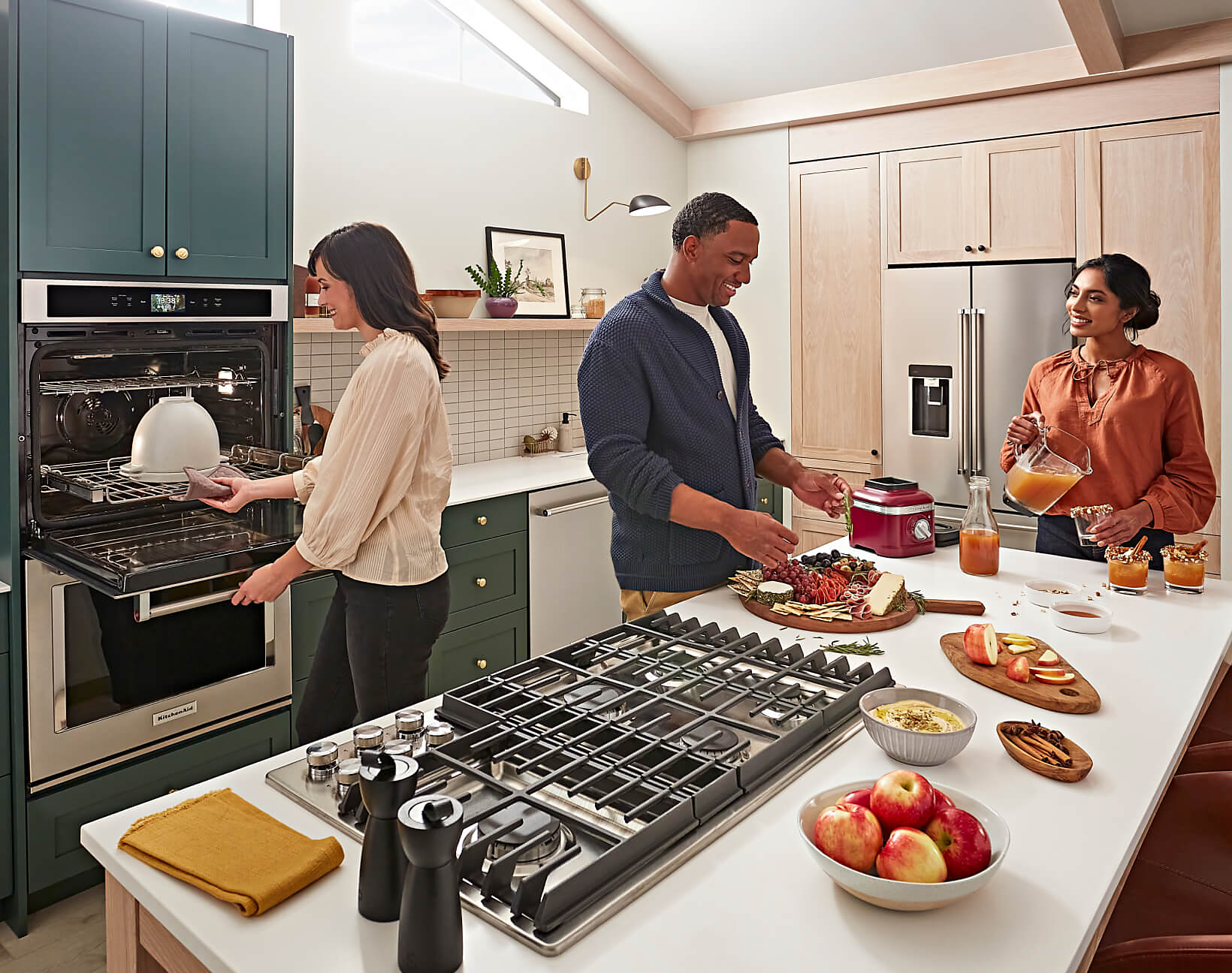 People gathering in a modern, stylish kitchen, preparing different charcuterie boards and other dishes with KitchenAid® appliances. 