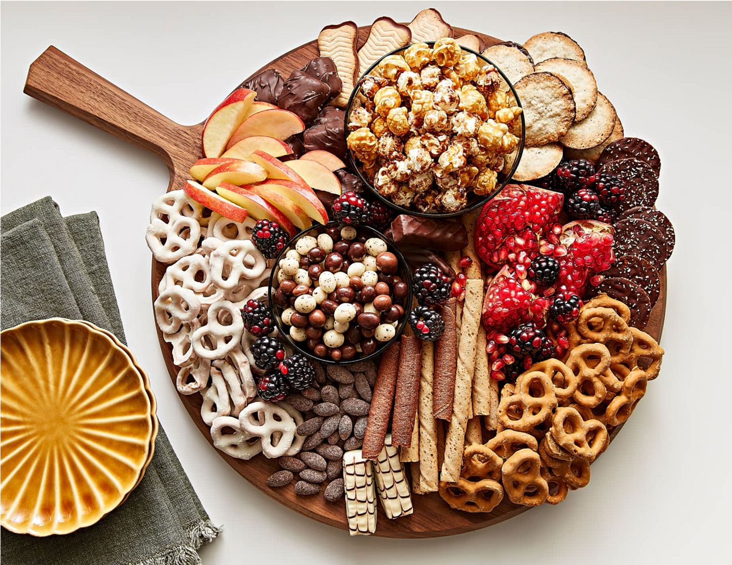 A dessert charcuterie board being filled with different sweets, fruits, nuts and other treats.