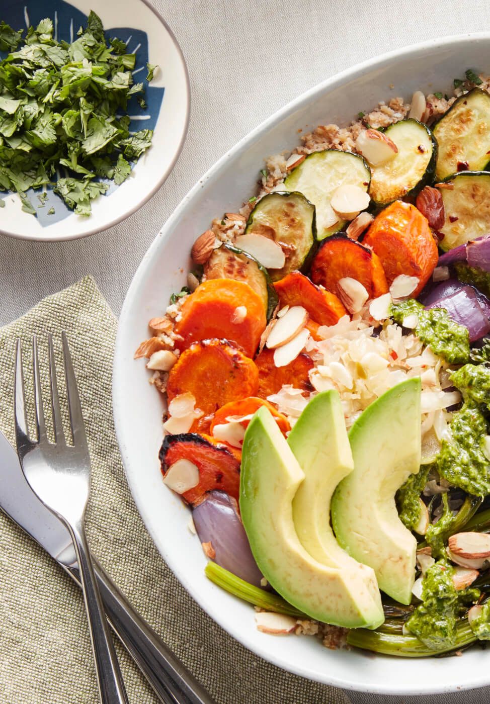 A white bowl filled with fresh avocado, carrots, cauliflower, zucchini, herbs, nuts and grains.
