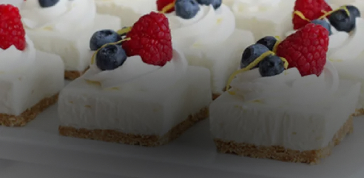 Bite-sized cheesecakes garnished with whip cream, strawberries and blueberries.