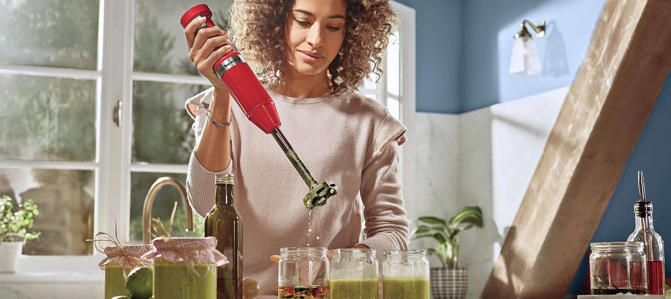 A young woman using an Empire Red Cordless Hand Blender to blend homemade green juice.
