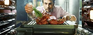 A view from inside an oven, as a man intently pulls out the grill attachment to add some finishing touches to a roast he’s preparing.
