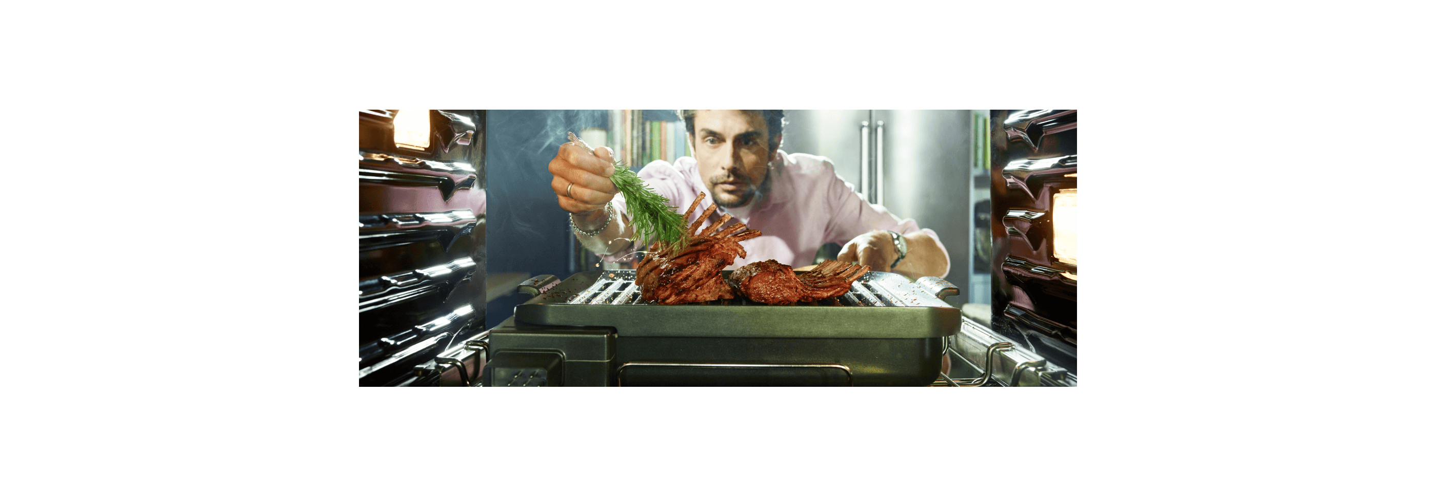 A view from inside an oven, as a man intently pulls out the grill attachment to add some finishing touches to a roast he’s preparing.